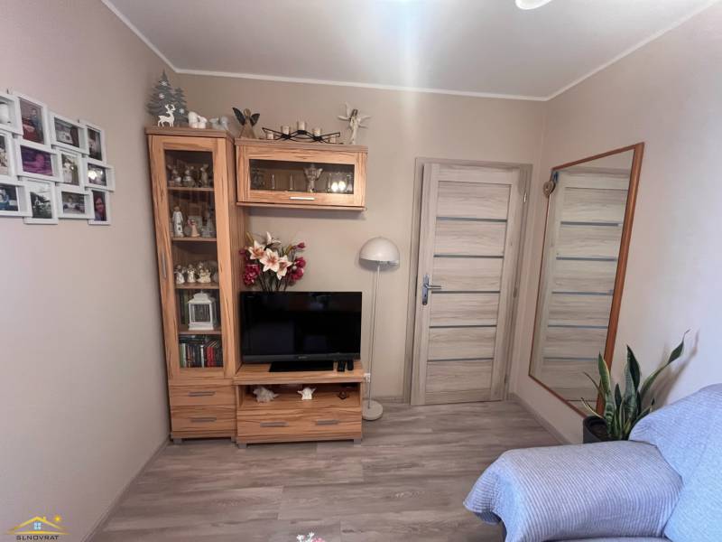 Pokoj s televizí, zrcadlem, dřevěnou sestavou a pohovkou, ve 3-pokojovém bytě.