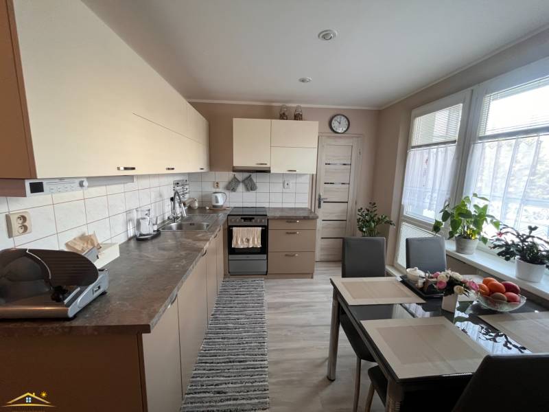 Kuchyně ve 3-pokojovém bytě se stolem, spotřebiči a rostlinami.