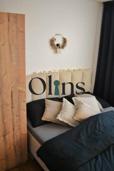 Ložnice v 3pokojovém bytě s dekorativním věncem a černými závěsy; postel s polštáři.