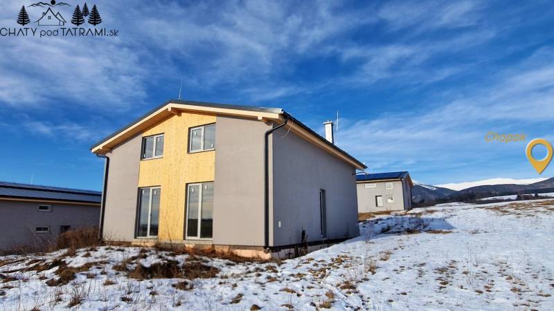 Chata v Dolní Lehotě s dřevěným obkladem, zasněžená krajina a hory na obzoru.