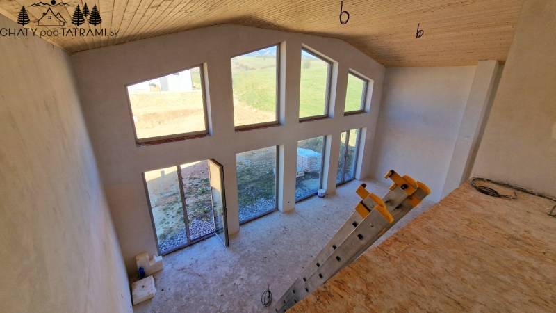 Interiér chaty s velkými okny, schody a podlahou s dřevěným dekorem.