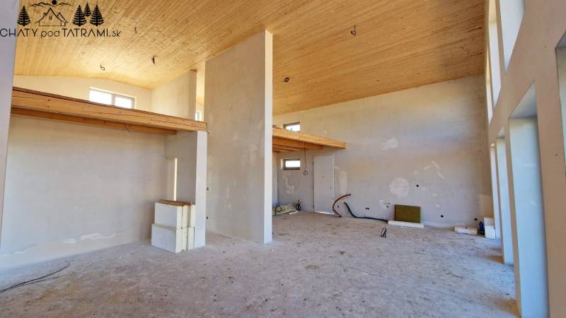 Interiér chaty s vysokým stropem, surově upravené stěny a jemné dřevěné dekorace.