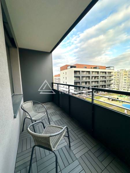 Balkon se dvěma židlemi a dlaždicemi s dřevěným dekorem, výhled na budovy.