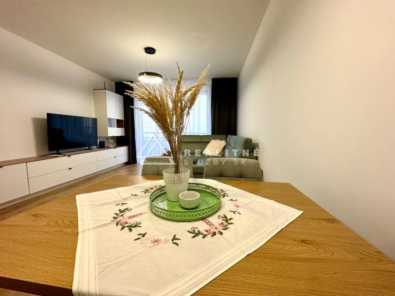 Obývací pokoj v 2-pokojovém bytě; pohovka, televizor, stůl s dekorací, podlaha s dřevěným dekorem.