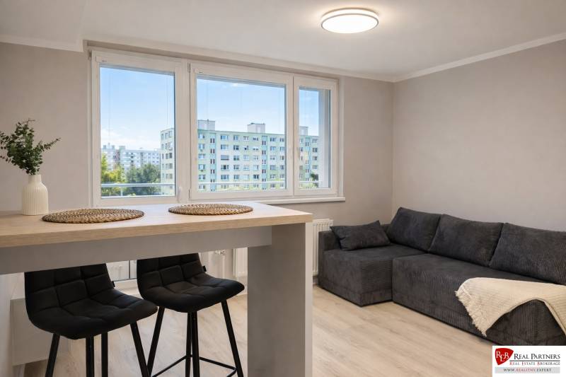 Obývací pokoj v dvoupokojovém bytě s pohovkou, barovým stolem a židlemi.