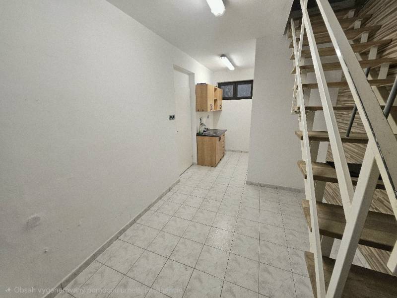 Interiér s bílými stěnami, kuchyňskou skříňkou, schodištěm a podlahou s dřevěným dekorem.