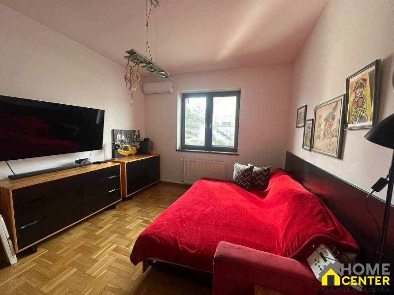 Ložnice v rodinném domě s červenou pohovkou, uměleckými díly a podlahou s dřevěným dekorem.