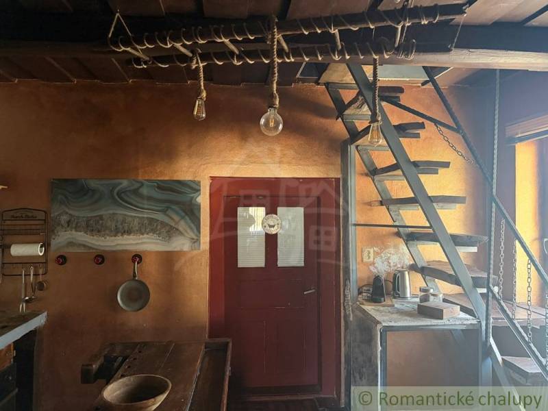 Interiér rodinného domu s dřevěnými schody, rustikálním stolem a uměleckou malbou na stěně.