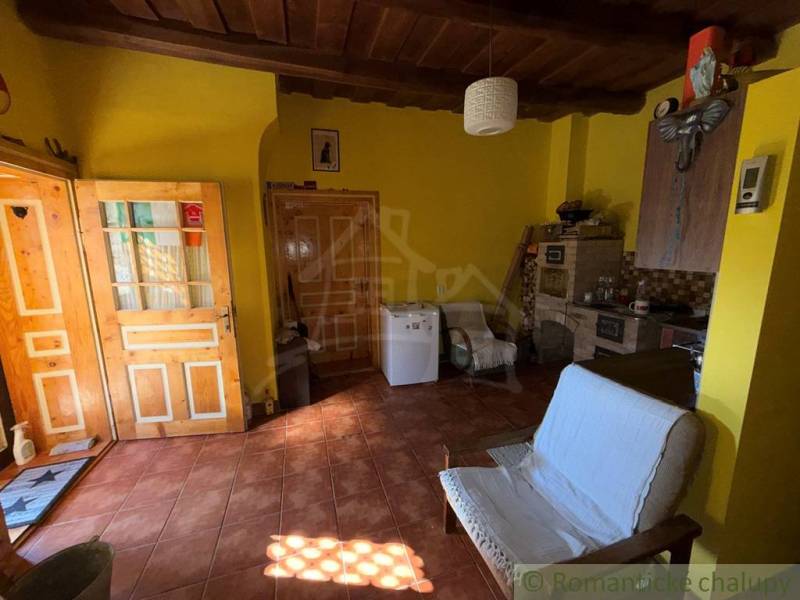 Pokoj v rodinném domě s cihlovou podlahou, dřevěným stropem a žlutými stěnami.