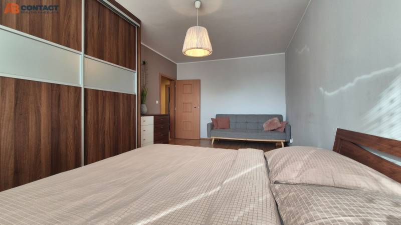 Ložnice v dvoupokojovém bytě s pohovkou, šatní skříní a podlahou s dřevěným dekorem.