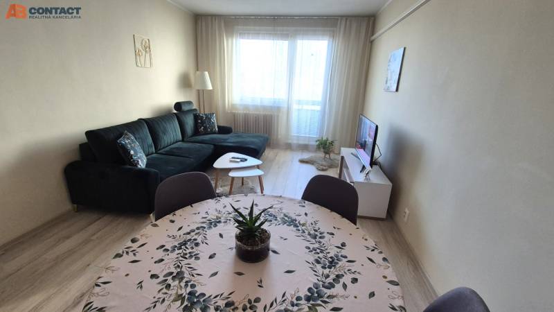 Obývací pokoj s tmavou sedačkou, jídelním stolem a podlahou s dřevěným dekorem v 2pokojovém bytě.