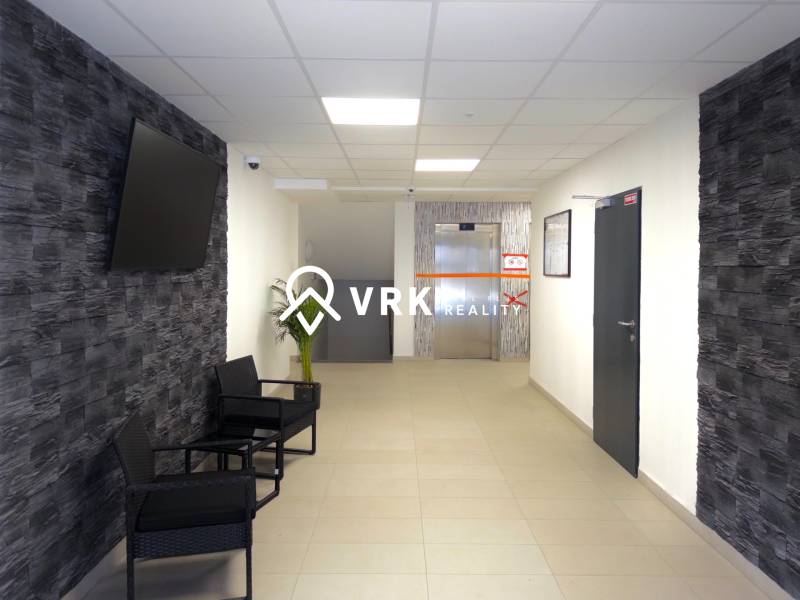 Předsíň v 3-pokojovém bytě s TV na stěně a výtahem v pozadí.