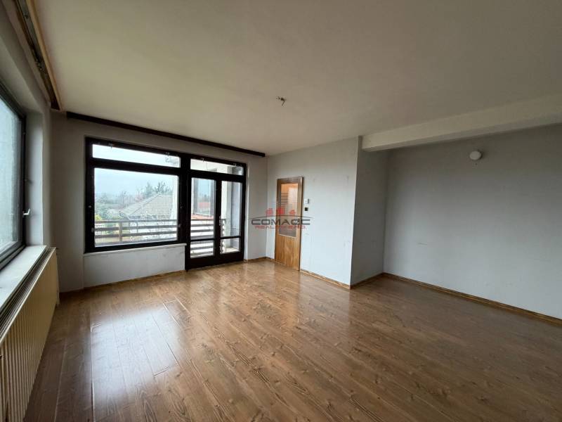 Pokoj v rodinném domě s podlahou s dřevěným dekorem a velkými okny do zahrady.