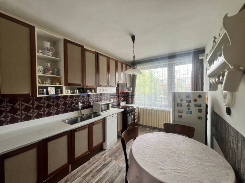 Kuchyně v rodinném domě s dřevěnými skříňkami, kulatým stolem a podlahou s dřevěným dekorem.