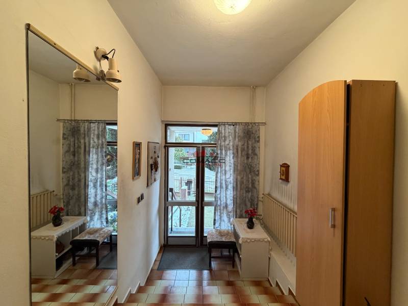 Interiér rodinného domu se zrcadlem, skříní, dlažbou a výhledem na zahradu.