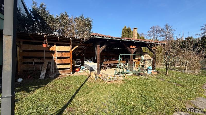 Zahrada rodinného domu v Lutile, s dřevěným přístřeškem a houpačkou na pozemku.