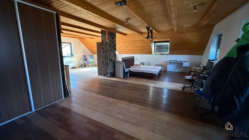 Podkrovní pokoj s postelí, skříní a podlahou s dřevěným dekorem v rodinném domě.