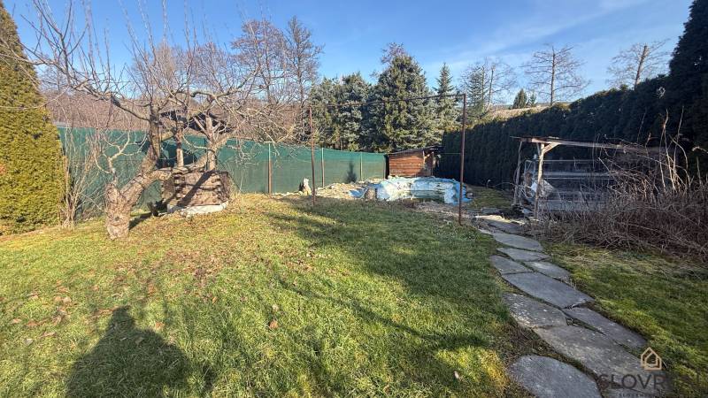 Zahrada rodinného domu v Lutile s dřevinami a chodníkem ve slunném prostředí.