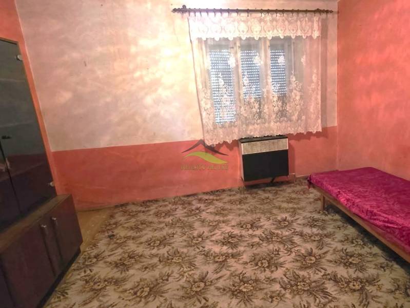 Pokoj v rodinném domě s kobercem, postelí a skříňkou, záclonou na okně.