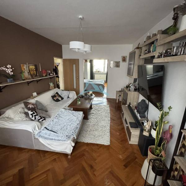 Obývací pokoj s pohovkou, stolem a podlahou s dřevěným dekorem ve 3pokojovém bytě.