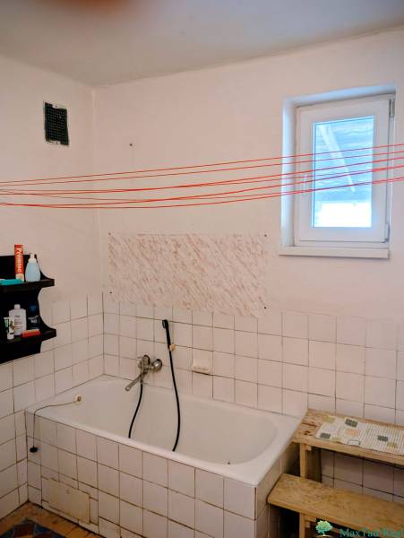 Koupelna v rodinném domě s vanou, poličkou a bílými kachličkami.