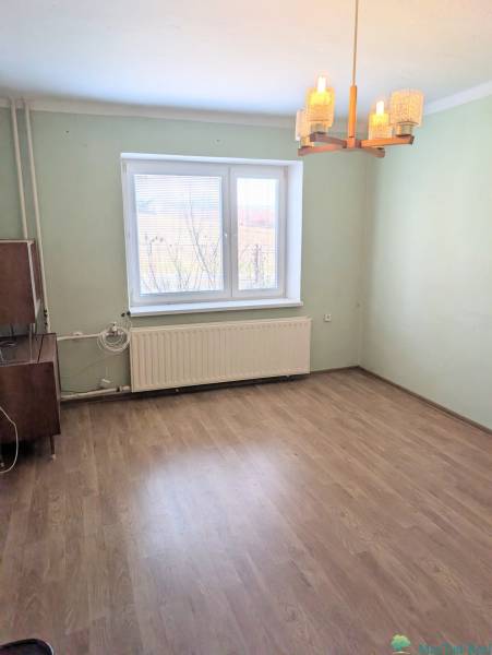 Pokoj v rodinném domě s podlahou s dřevěným dekorem a oknem s radiátorem.