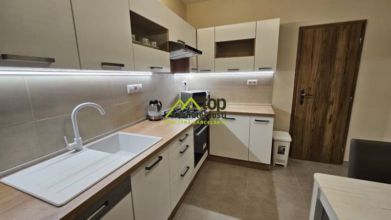 Kuchyně v 2-pokojovém bytě s bílými skříňkami a podlahou s dřevěným dekorem.