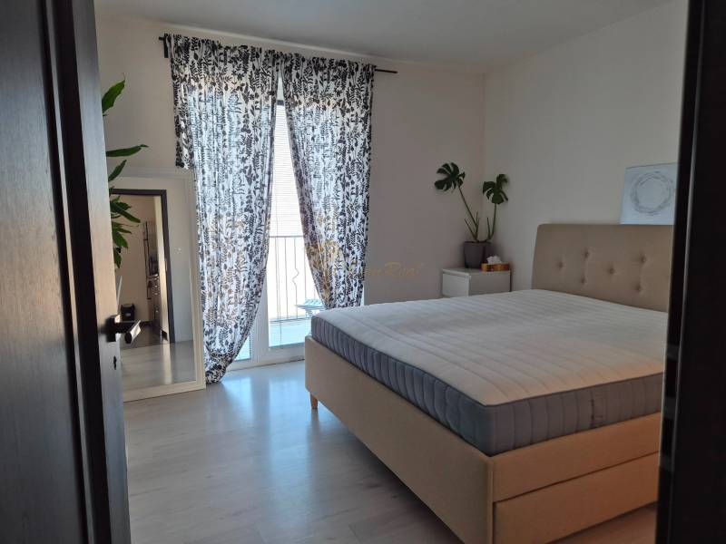 Ložnice s velkou postelí, rostlinami, zrcadlem a závěsy ve 3-pokojovém bytě.