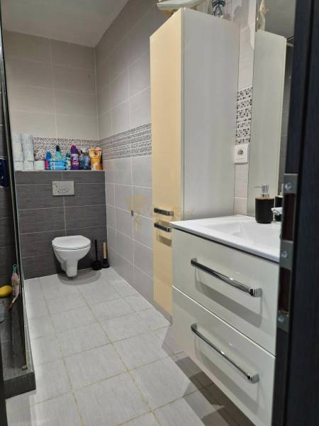 Koupelna v 3pokojovém bytě se závěsným WC, umyvadlem, skříňkou a světlými obklady.