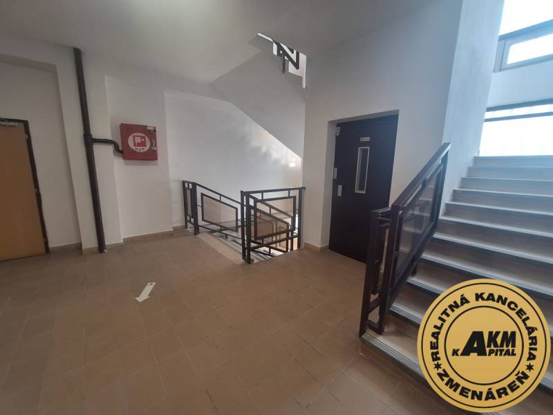 Schodiště v kancelářích s dlažbou a výtahem. Na stěně nouzový box.