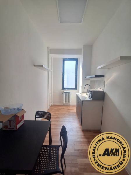 Úzká kancelář s černým stolem, židlemi a podlahou s dřevěným dekorem.