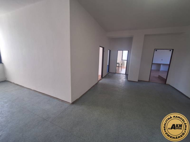 Interiérová fotografie prostoru se světlými stěnami a třemi dveřmi, podlaha s dřevěným dekorem.