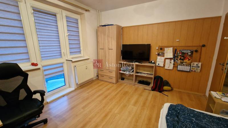 Pokoj v 3-pokojovém bytě s podlahou s dřevěným dekorem, televizorem a křeslem.