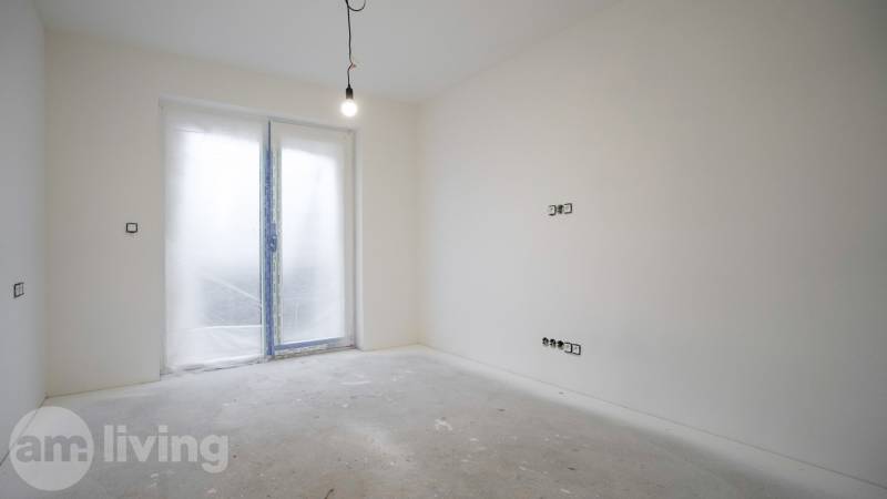 Prázdná místnost v rodinném domě se závěsnou žárovkou a zavřenými dveřmi na terasu.