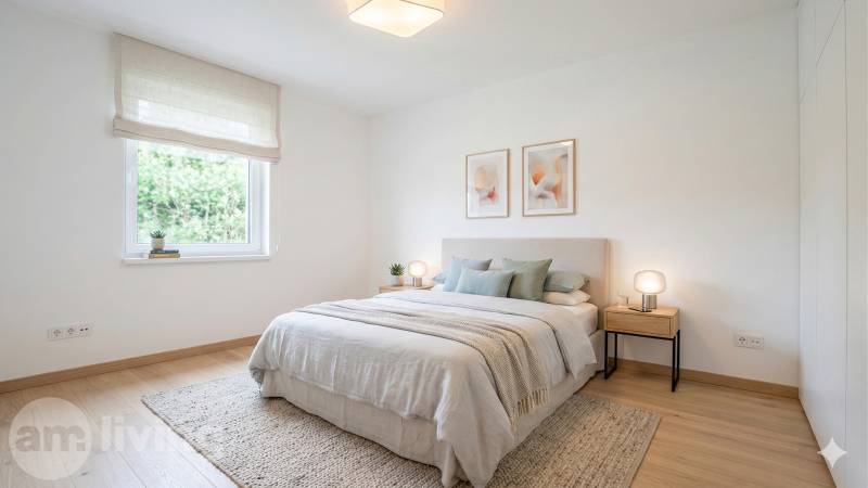 Světlá ložnice s podlahou s dřevěným dekorem, postel se světlým přehozem a obrazy na stěně.