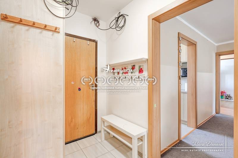 Vstupní chodba ve 4pokojovém bytě, bílé stěny, věšáky a lavice.