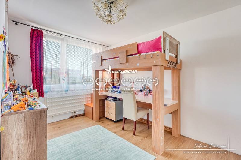 Dětský pokoj s vyvýšenou postelí, podlahou s dřevěným dekorem a hračkami na policích.