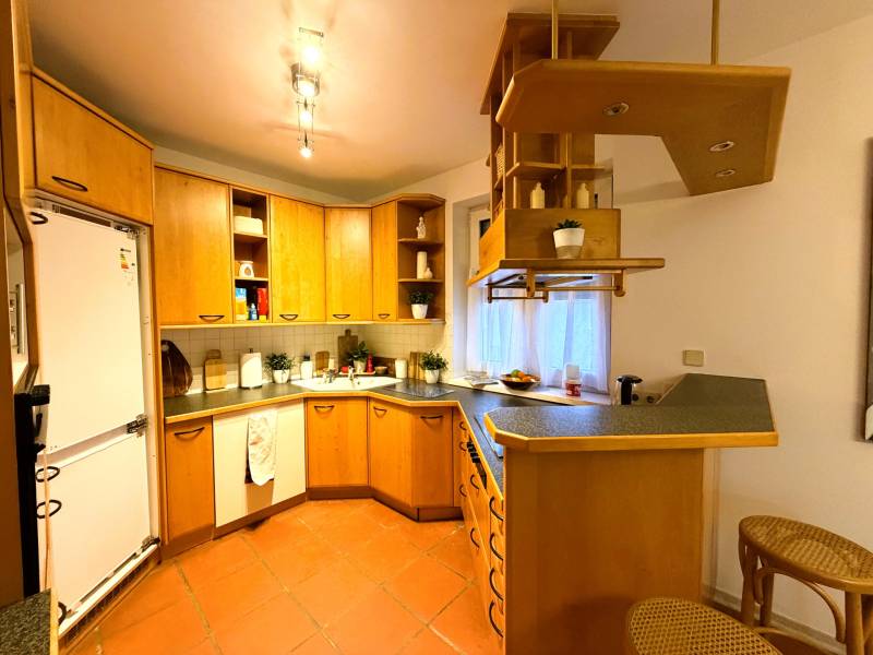 Kuchyně v 3-pokojovém bytě s dřevěnými skříňkami a barovým pultem.