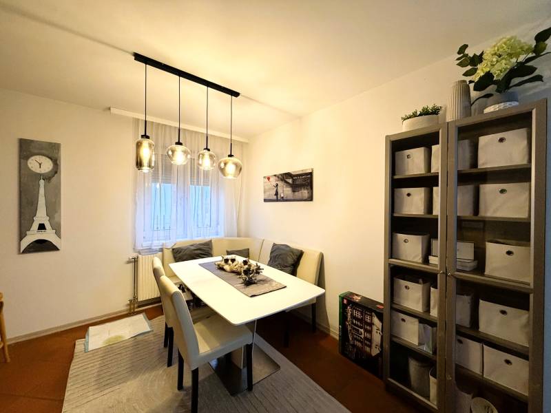 Jídelna se stolem, židlemi a regálem v 3-pokojovém bytě s dekorativním osvětlením.