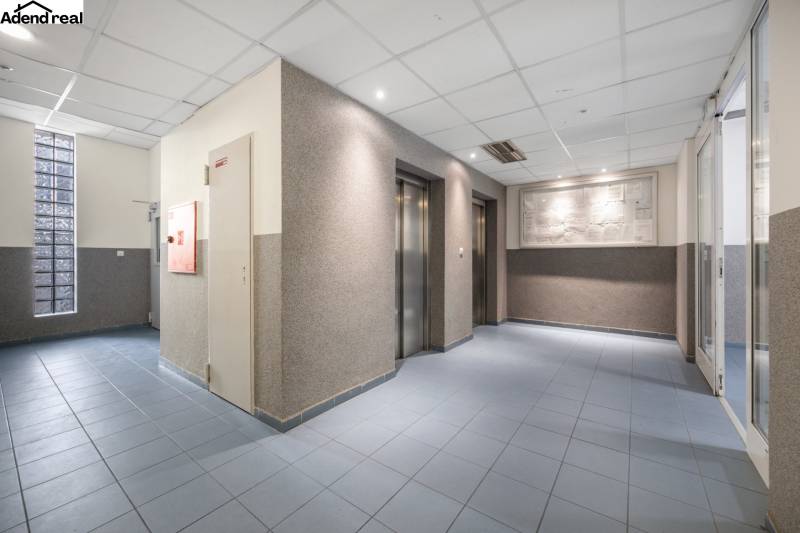 Vstupní hala s výtahy, modrá podlaha, osvětlené stropy.