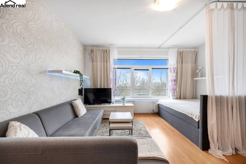 Obývací pokoj s pohovkou, závěsem a televizí, podlaha s dřevěným dekorem.