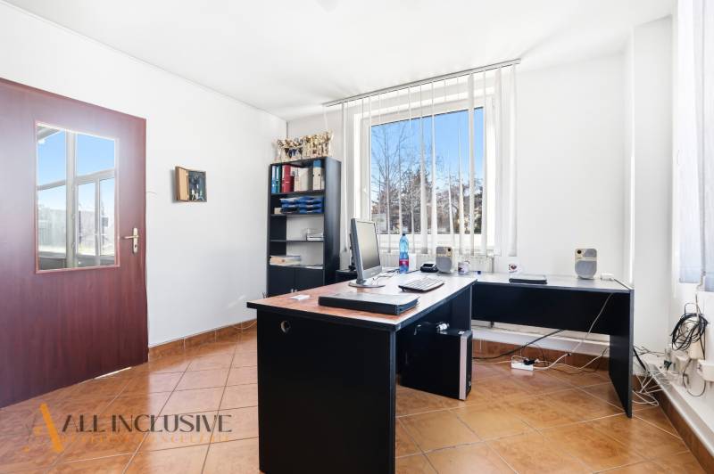 Kancelář s počítačem, policí a oknem s vertikálními žaluziemi v obchodních prostorách.