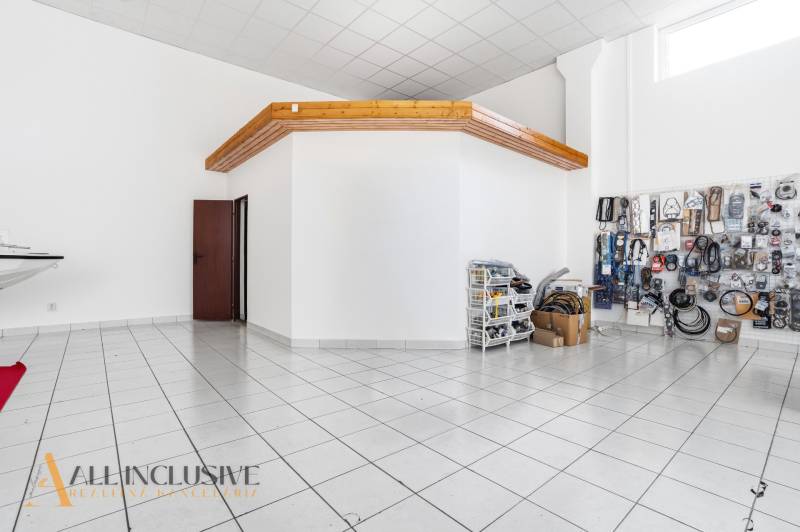 Obchodní prostory s bílými stěnami a keramickou podlahou. Součástí je uložené zboží.