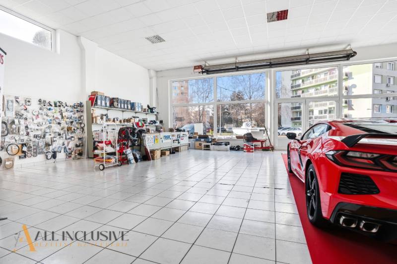 Autoservisní obchodní prostory se sklem a vystaveným autem na dlažbě, součástky na stěnách.