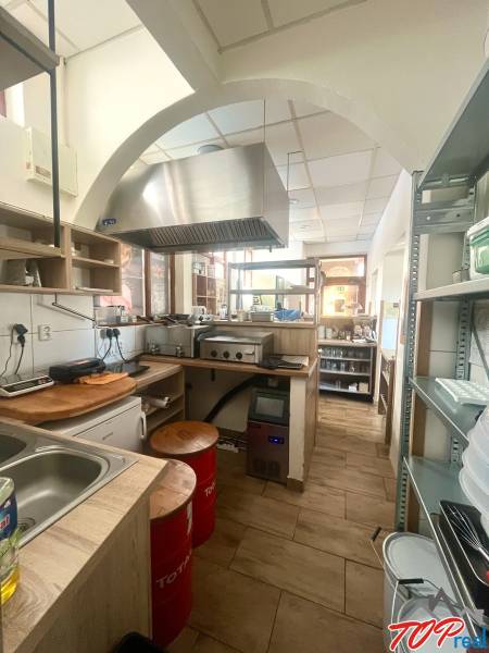 Gastro prostory s dřevěným dekorem, kuchyňská linka, odsavač par, spotřebiče, police, židle.