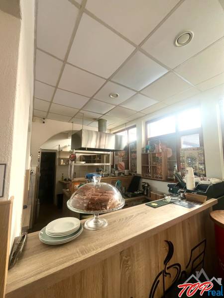 Interiér gastro prostoru s podlahou s dřevěným dekorem, pultem, zákuskem a talíři.