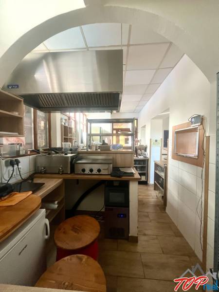 Kuchyňský prostor s nerezovým digestořem a podlahou s dřevěným dekorem v gastro prostorech.