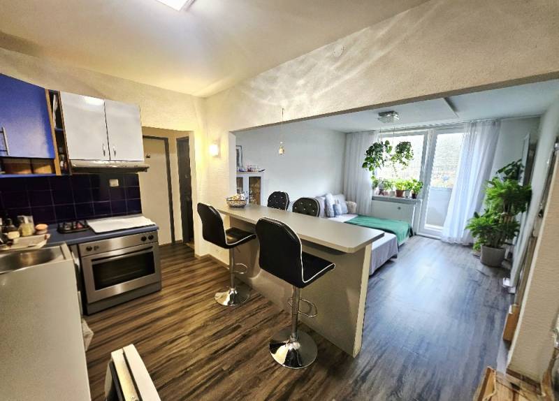 Kuchyně s propojením na obývací pokoj a podlahou s dřevěným dekorem ve 3pokojovém bytě.