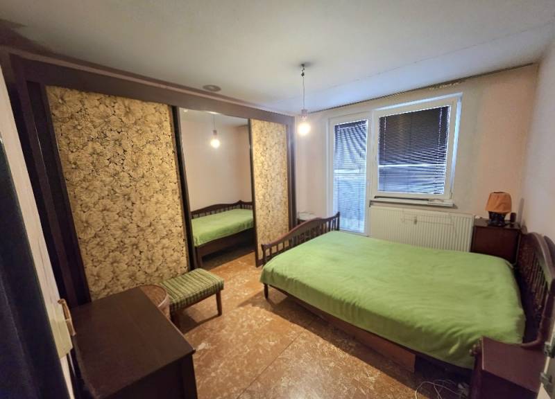 Ložnice ve 3pokojovém bytě s velkou skříní, postelí a zeleným povlečením na posteli.