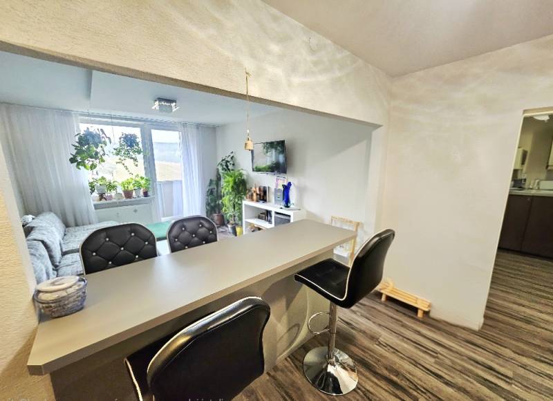 3pokojový byt s barovým pultem a pohodlným posezením, podlaha s dřevěným dekorem.